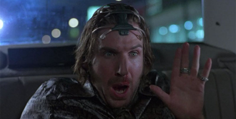 Lenny sitting in a the back sit of a car wearing the SQUID device with a face of horror.